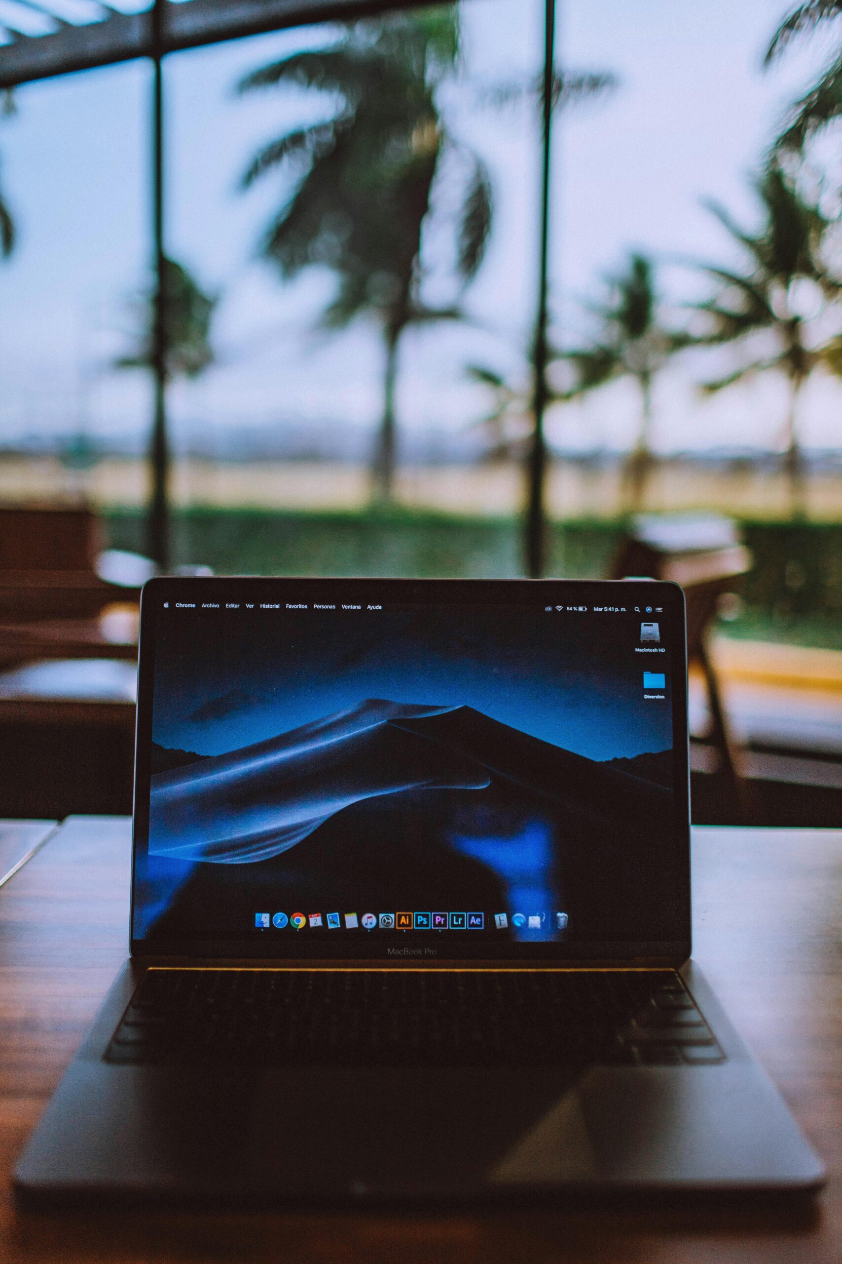 A sleek laptop on a wooden desk with a tropical view behind, ideal for remote work and travel themes.